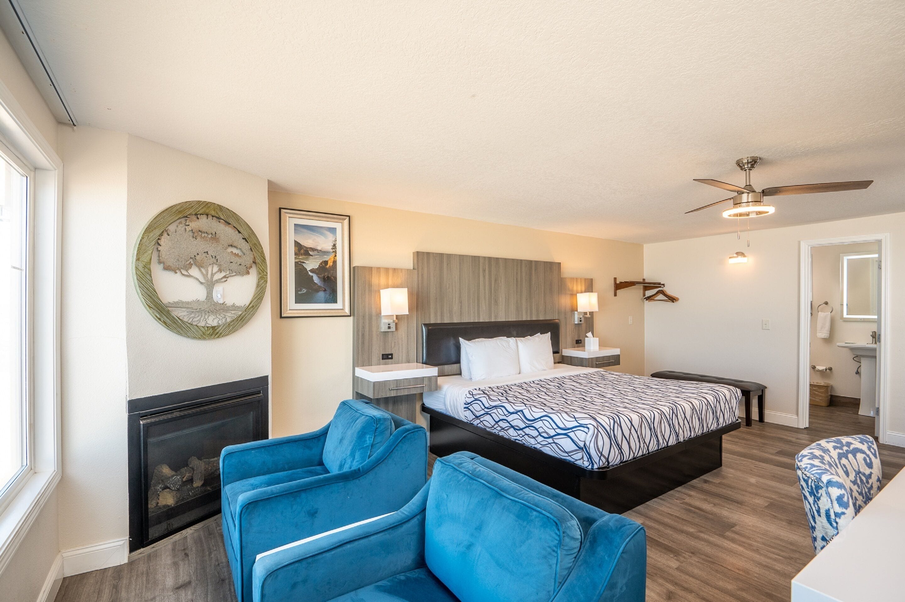 A hotel room with a large bed, a fireplace, a ceiling fan, and a blue armchair.