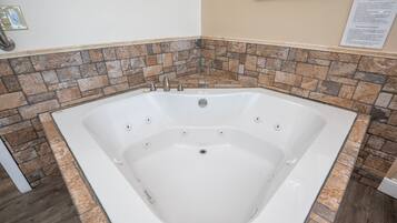 Eine große, weiße, freistehende Badewanne mit Bordüre aus Steinmosaik, einer an der Wand montierten Leuchte und einem Hinweisschild im Bilderrahmen.