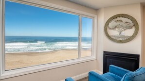A room with a large window overlooking a beach, a fireplace, and blue upholstered furniture.