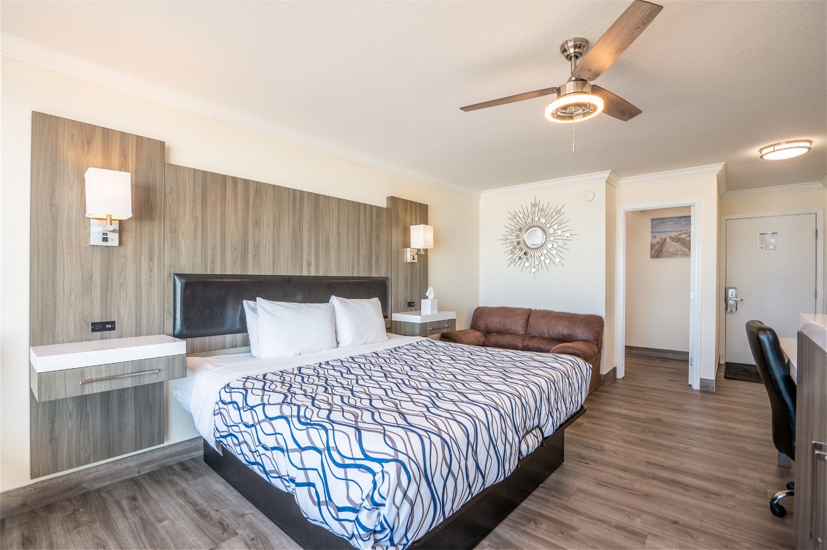 A modern bedroom with a large bed, a ceiling fan, bedside lamps, a brown leather chair, and a desk with a chair.