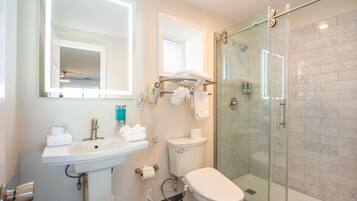 Un baño moderno con cabina de ducha de vidrio, un lavabo blanco con espejo encima y un inodoro.