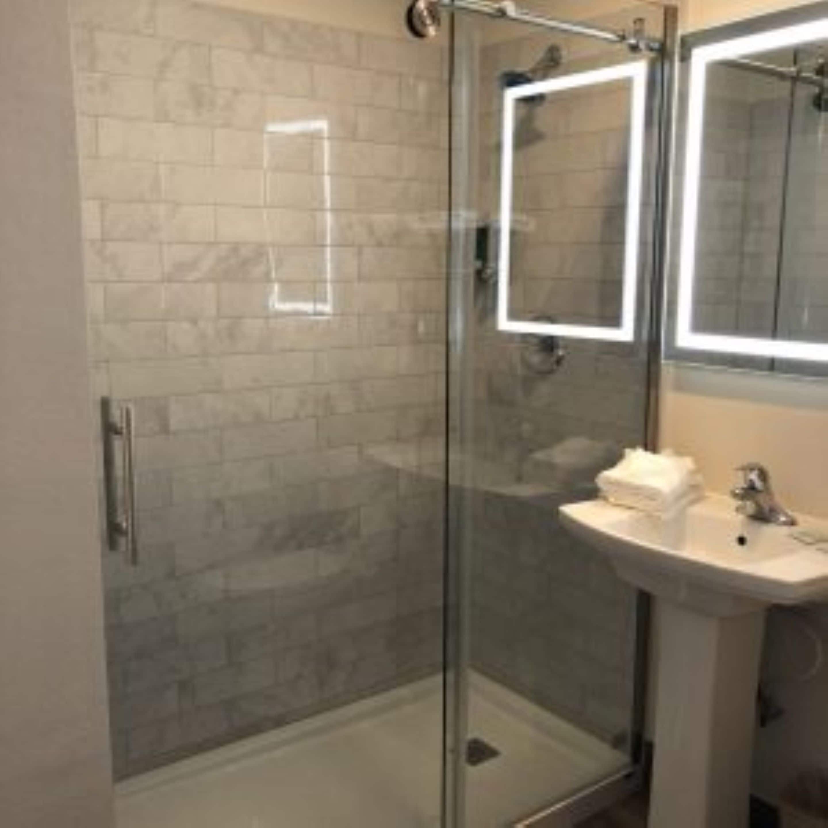 Un baño con ducha de vidrio, un lavabo con espejo y paredes de azulejos.