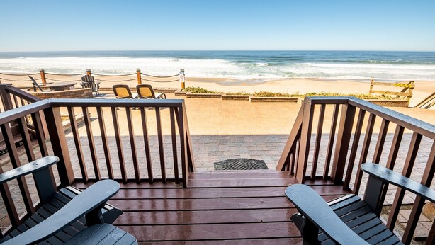 A wooden deck with chairs overlooking a beach.