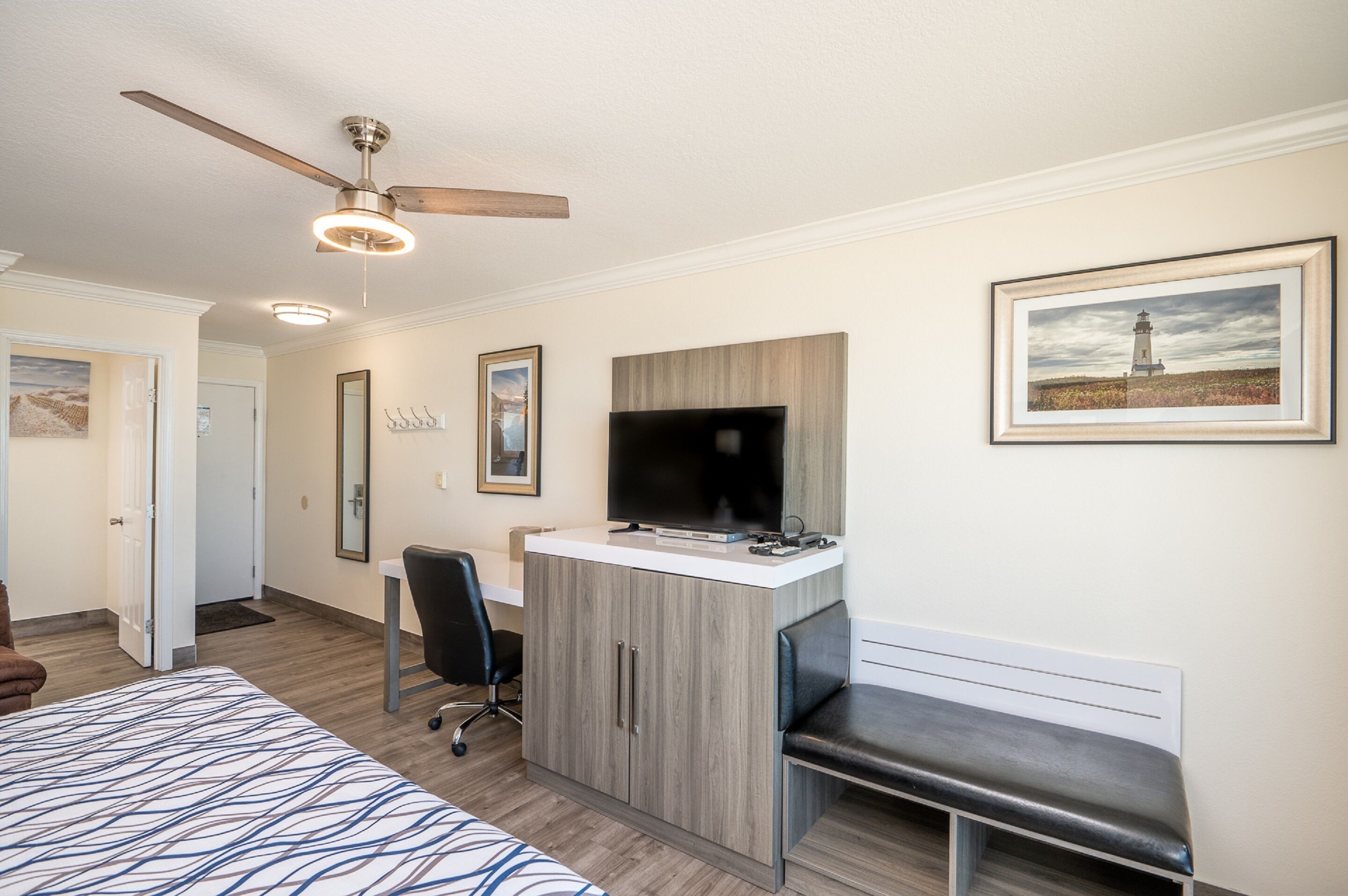 Ein Schlafzimmer mit Bett, Schreibtisch, Stuhl, Bank, Deckenventilator und Bildern an der Wand.