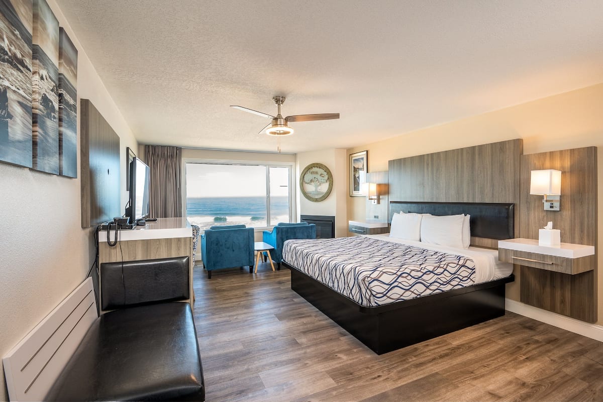 A modern hotel room with a large bed, a desk, a chair, a vanity, and a view of the ocean.
