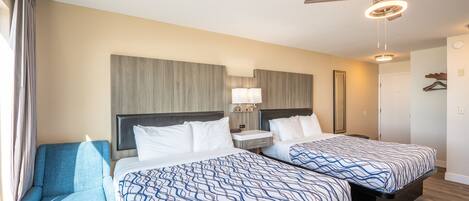 A hotel room with two beds, a chair, a ceiling fan, and a nightstand with a lamp.