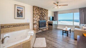 A modern bathroom with a bathtub, a stone accent wall, a mounted TV, and a view of the ocean through large windows.