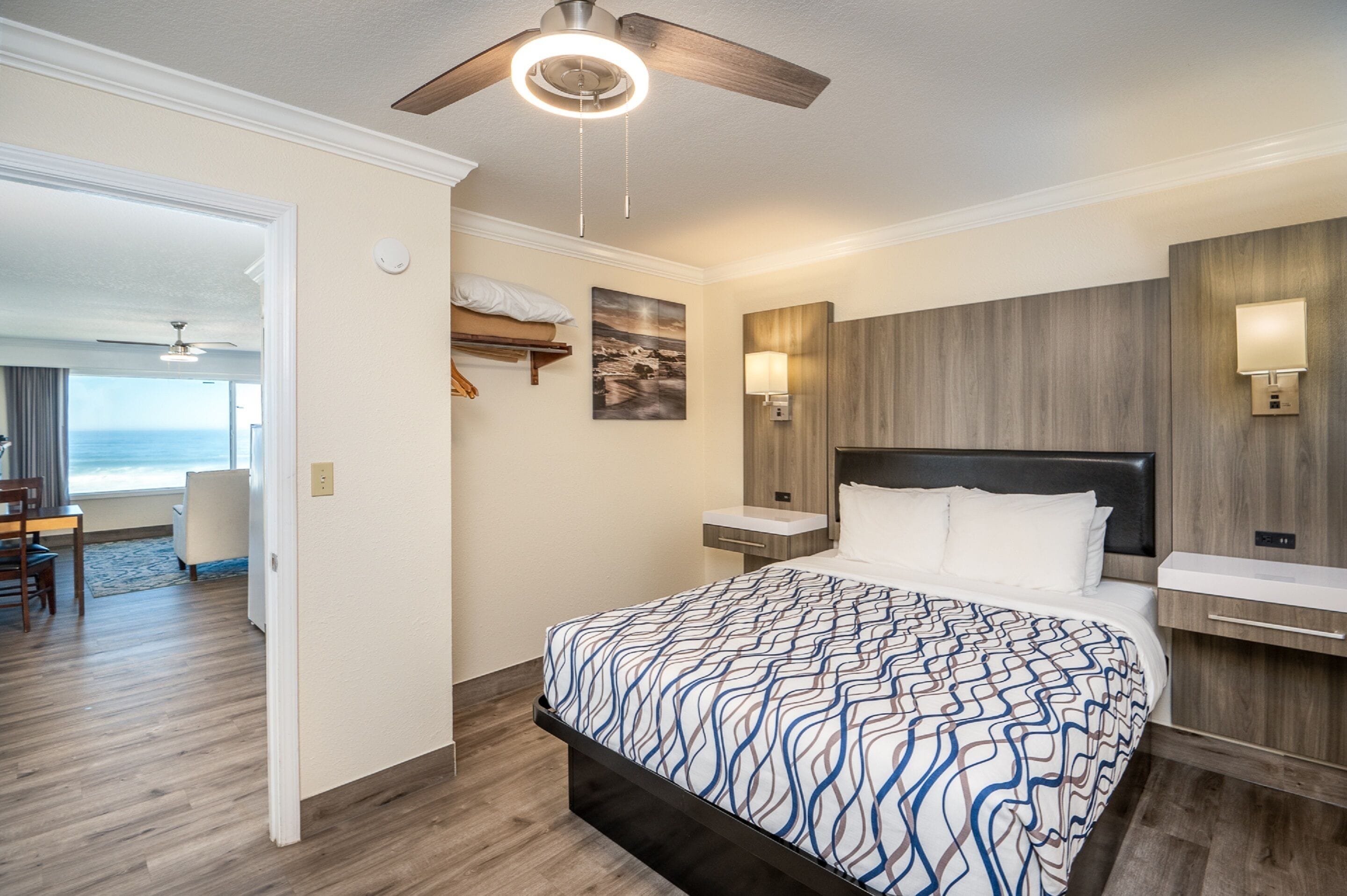 Une chambre d’hôtel avec un grand lit, un ventilateur de plafond, une table de chevet et une vue sur l’océan.
