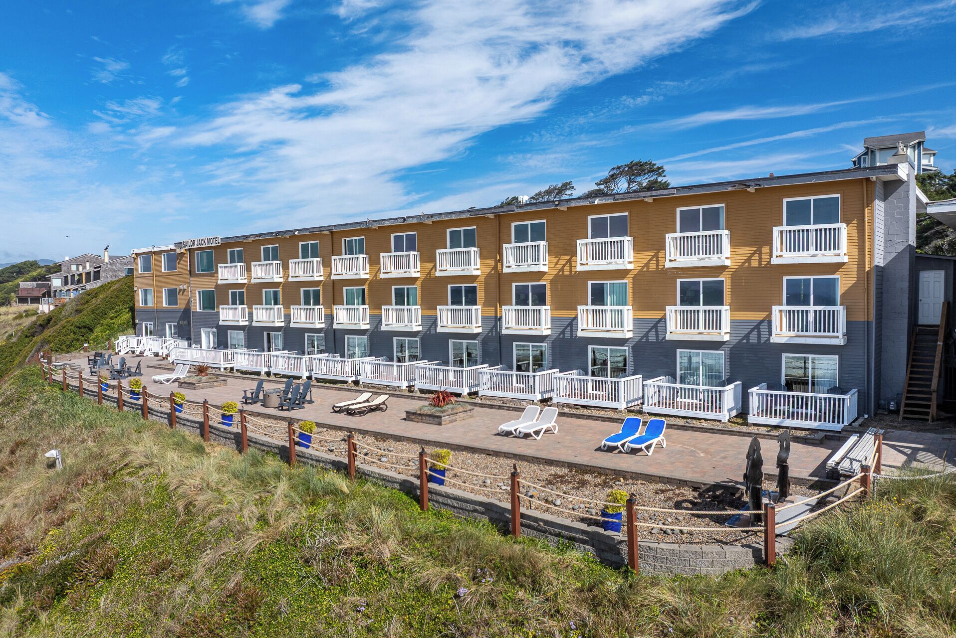 A multi-story hotel with balconies, a pool area with sun loungers, and a beach view.
