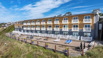 A multi-story hotel with balconies, a pool area with sun loungers, and a beach view.