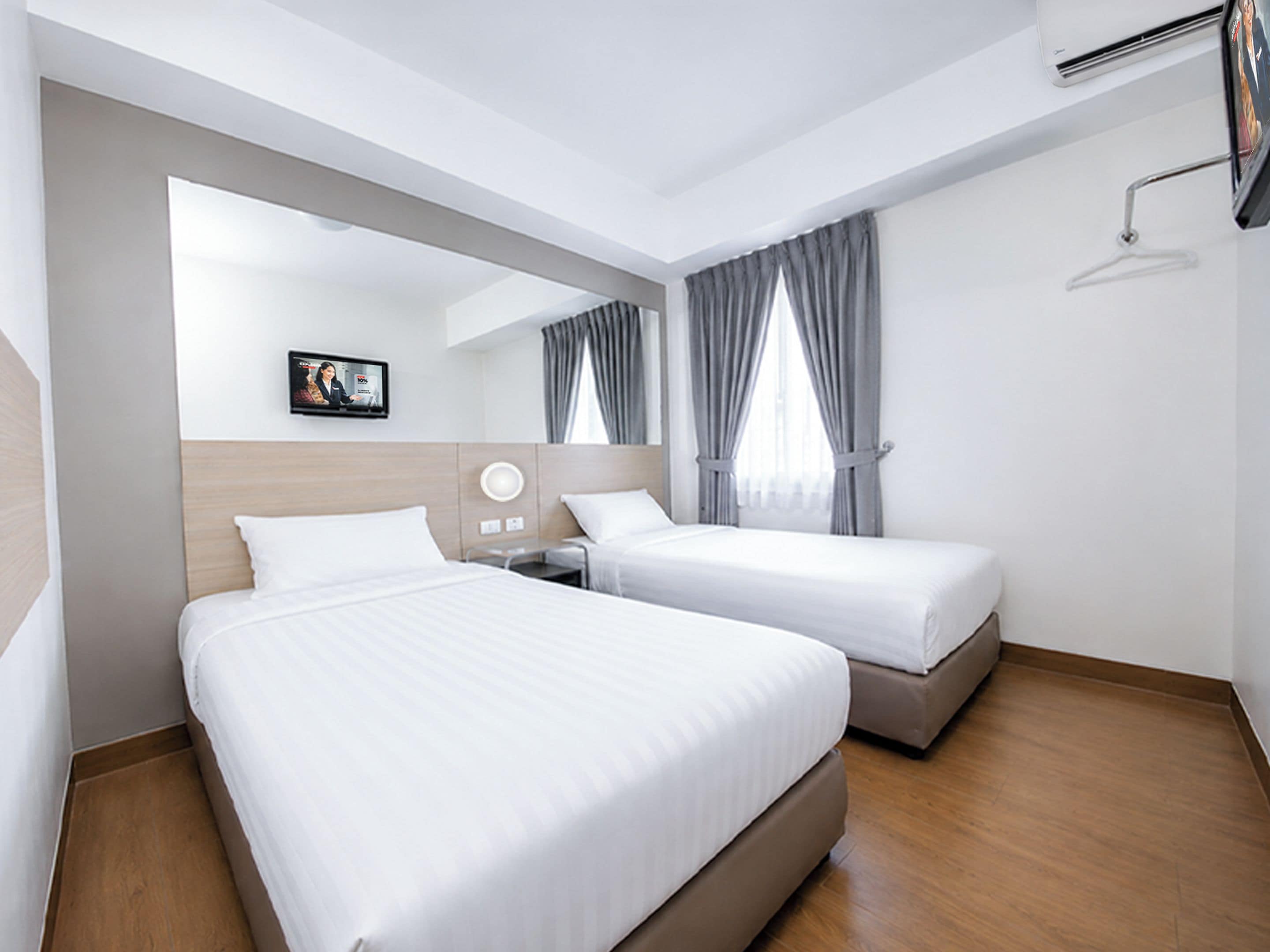 A hotel room with two beds, a flat-screen TV mounted on the wall, and a window with curtains.