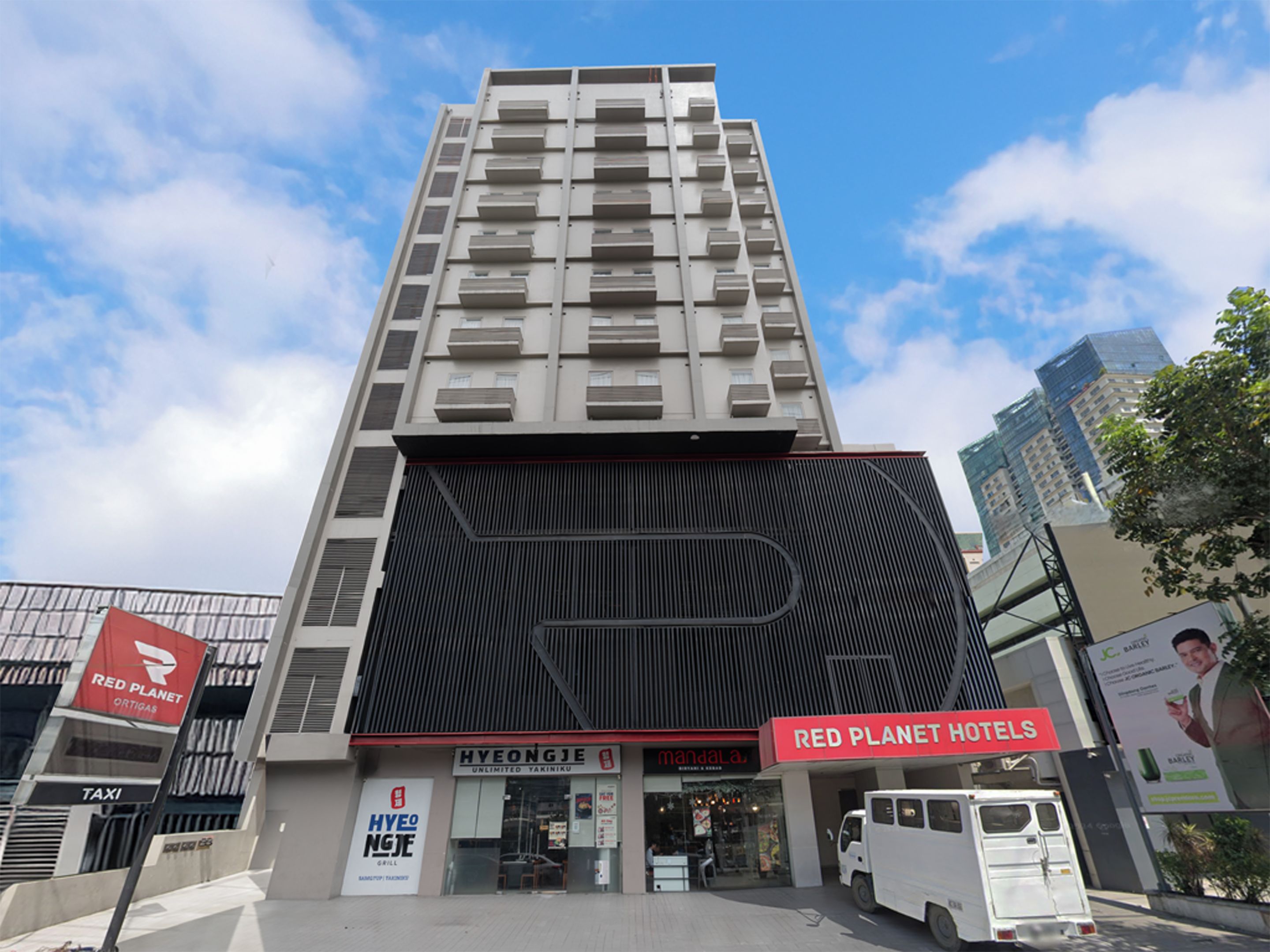 Um hotel moderno com um letreiro chamativo da Red Planet Hotels, entrada visível e um ponto de táxi.