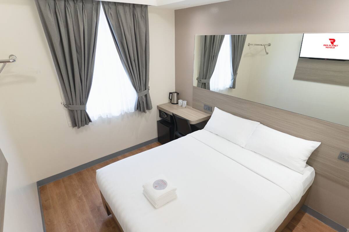 Quarto de hotel com uma cama grande, uma escrivaninha, uma cadeira, uma cafeteira e um espelho.