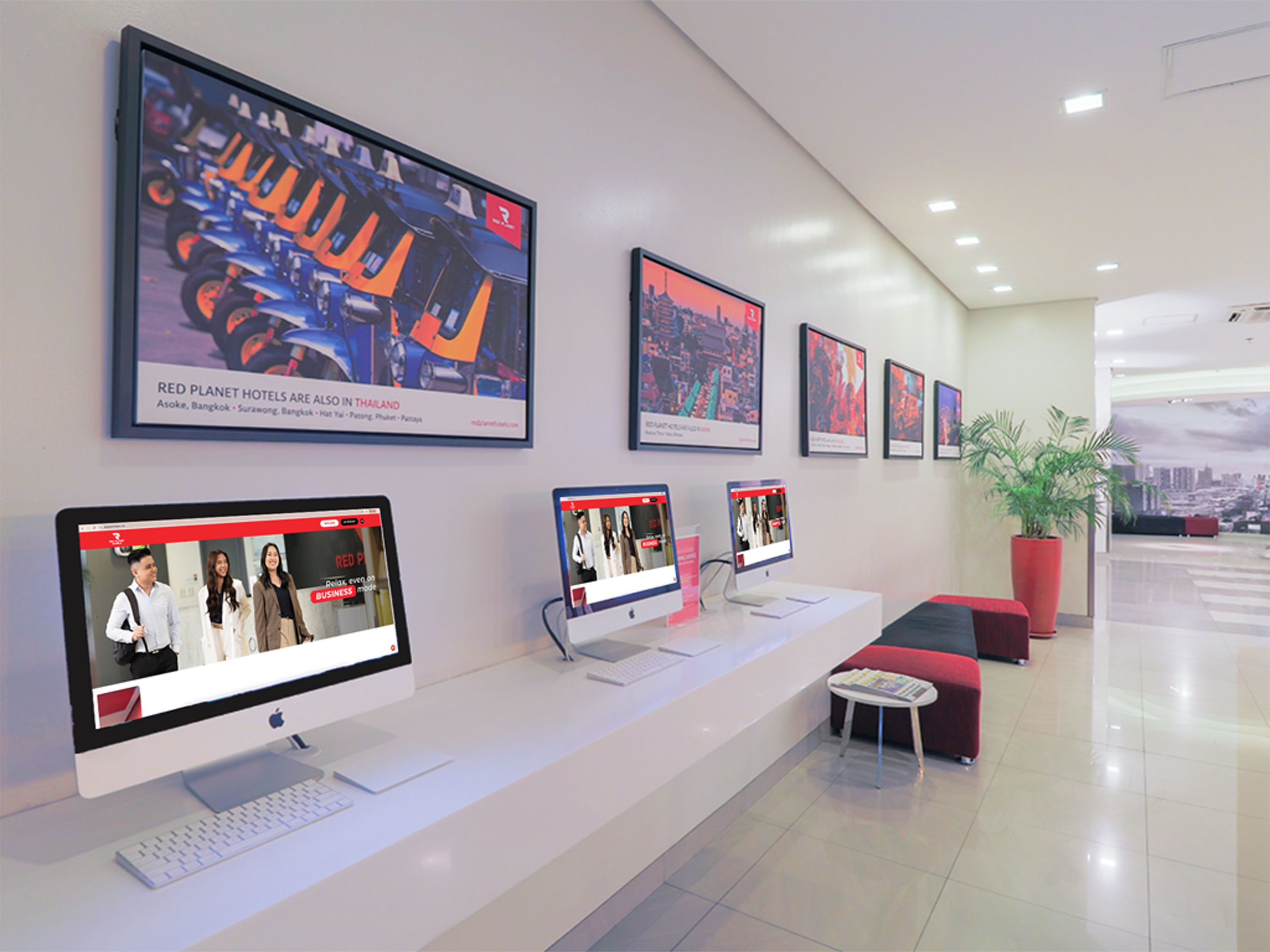 A reception area with multiple monitors displaying content, a reception desk, seating area, and framed cityscape pictures on the wall.