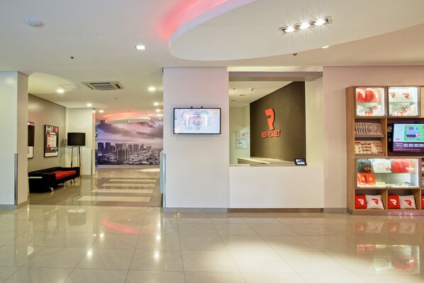 Un hall d’hôtel moderne avec un comptoir d’accueil, une fresque représentant un paysage urbain et une exposition sur le thème de la planète rouge.