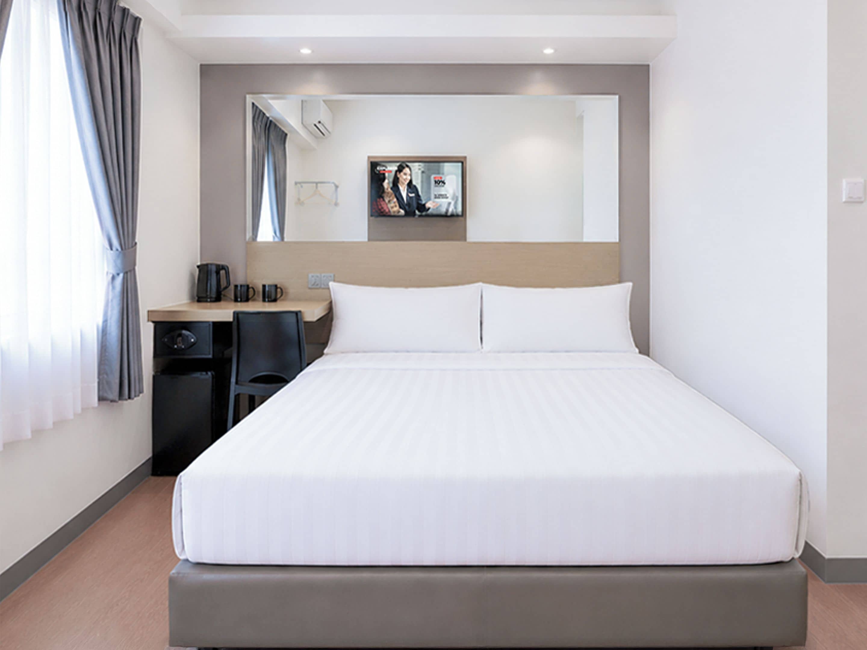 A hotel room with a large bed, a desk with a chair, a coffee maker, and a mirror on the wall.