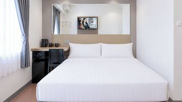 A hotel room with a large bed, a desk with a chair, a coffee maker, and a mirror on the wall.