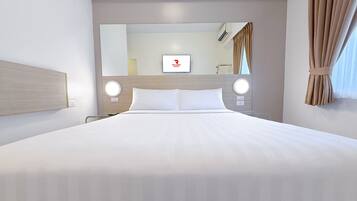 A hotel room with a large bed, two bedside tables, a round mirror, and a television on the wall.