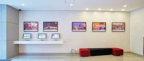 A modern reception area with a bench, three monitors, and cityscape artwork on the wall.