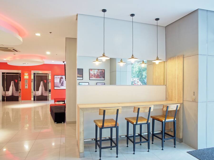 Un moderno vestíbulo de hotel con un mostrador de recepción, dos taburetes de bar e iluminación colgante.