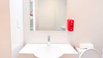 A bathroom with a white sink, a mirror, a red soap dispenser, and a white toilet.