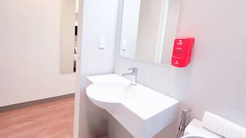 A modern bathroom with a white sink, a mirror, and a red soap dispenser.