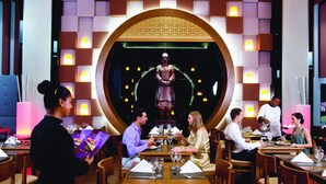 A restaurant with multiple dining tables, a central decorative arch, and a waiter serving guests.