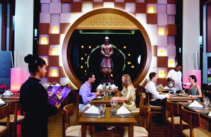 A restaurant with multiple dining tables, a central decorative arch, and a waiter serving guests.