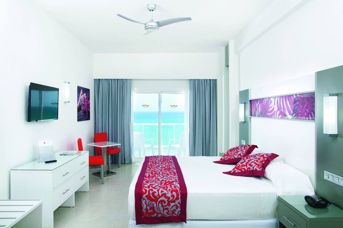 A hotel room with a bed, desk, chair, and a balcony with a view.