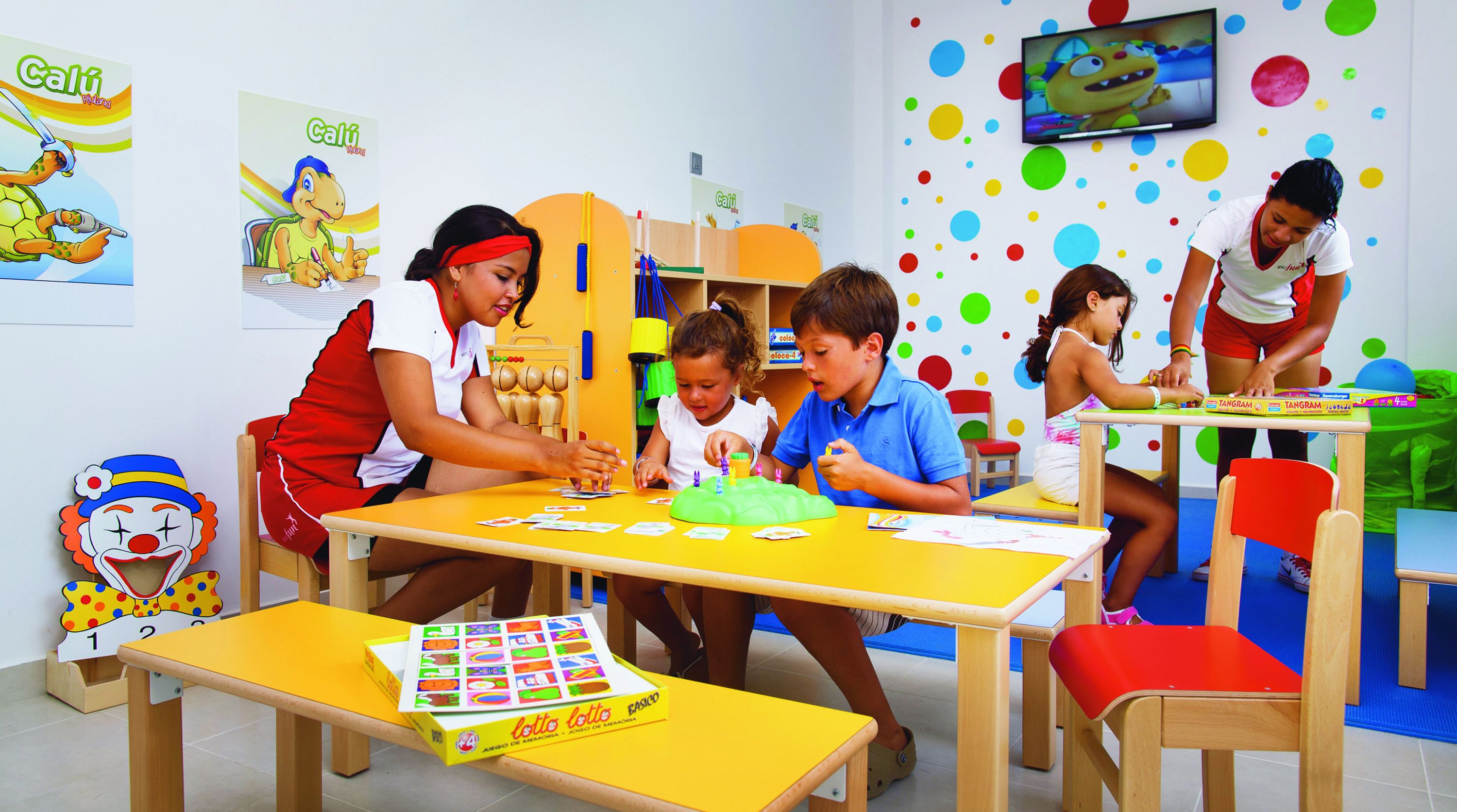 A classroom with children engaged in activities, colorful educational posters, and a television on the wall.