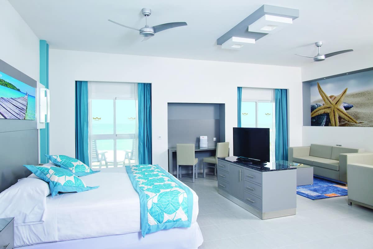 A hotel room with a bed, desk, TV, and a large window with curtains.