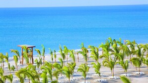 A beach with palm trees, a wooden structure, and white lounge chairs. - Hotel Riu Playa Blanca - All Inclusive (Rio Hato)
