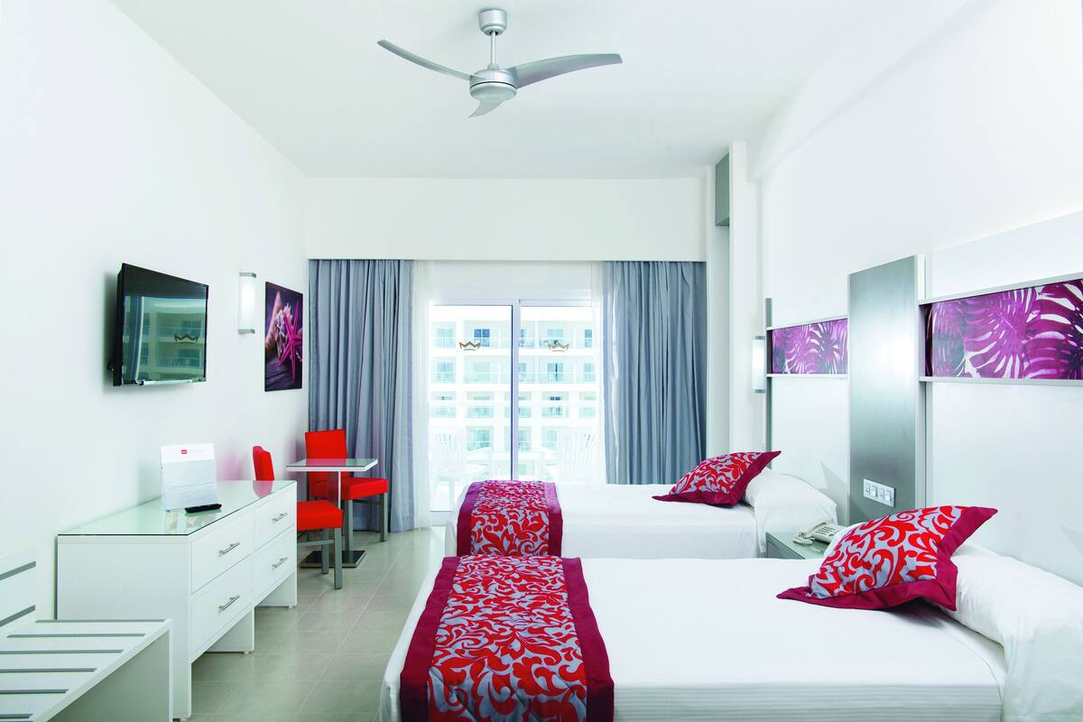 A modern hotel room with two beds, a desk, a chair, and a TV.