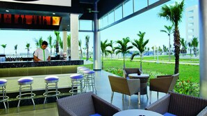 A modern bar area with a bartender, bar stools, and outdoor seating with wicker furniture. - Hotel Riu Playa Blanca - All Inclusive (Rio Hato)