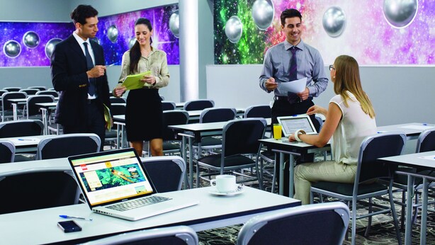 A conference room with tables, chairs, and a laptop displaying a webpage.