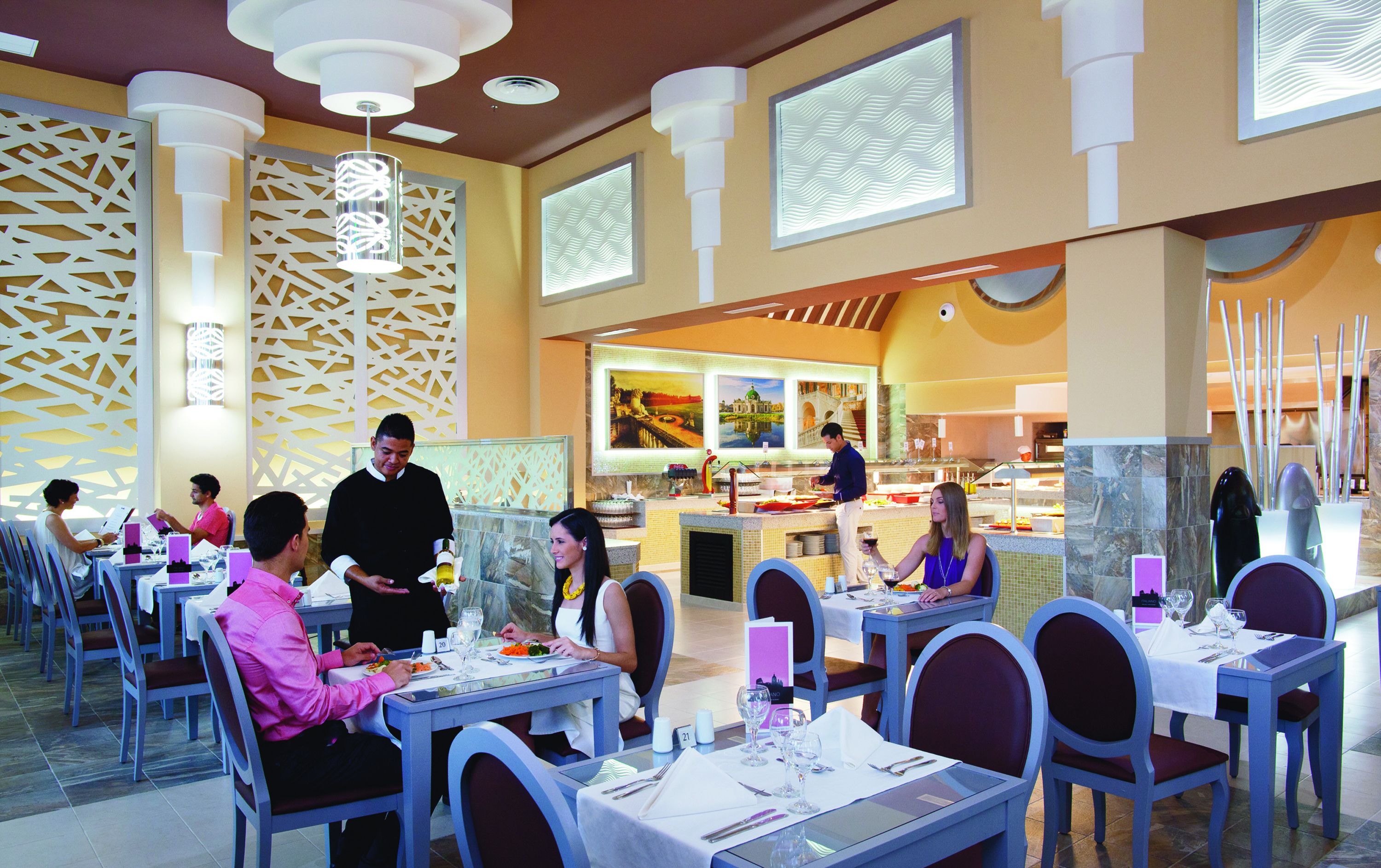 A restaurant with tables set for dining, a bar area, and a view of the kitchen.