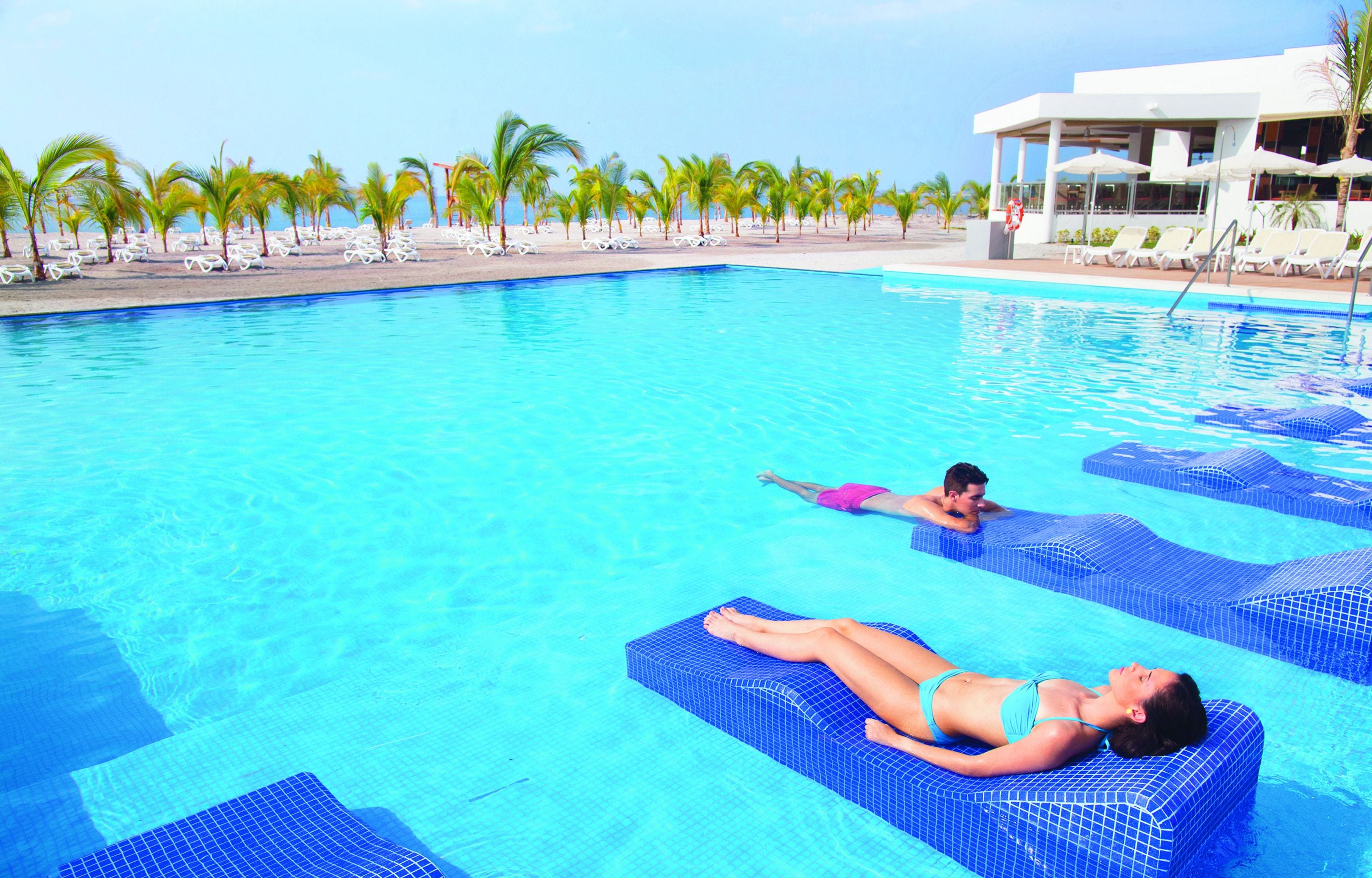A swimming pool with lounge chairs and palm trees.