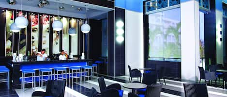 A modern restaurant with blue bar stools, black wicker chairs, and a large window offering a view of palm trees.
