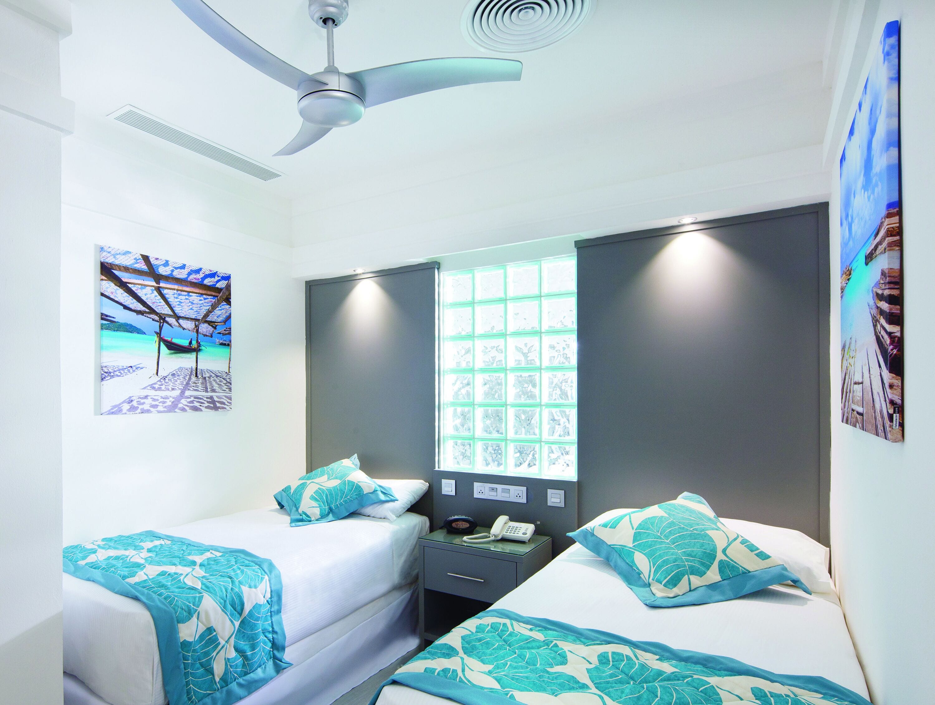 Une chambre d’hôtel avec deux lits, un ventilateur de plafond, une fenêtre donnant sur un beau paysage et un tableau accroché au mur.