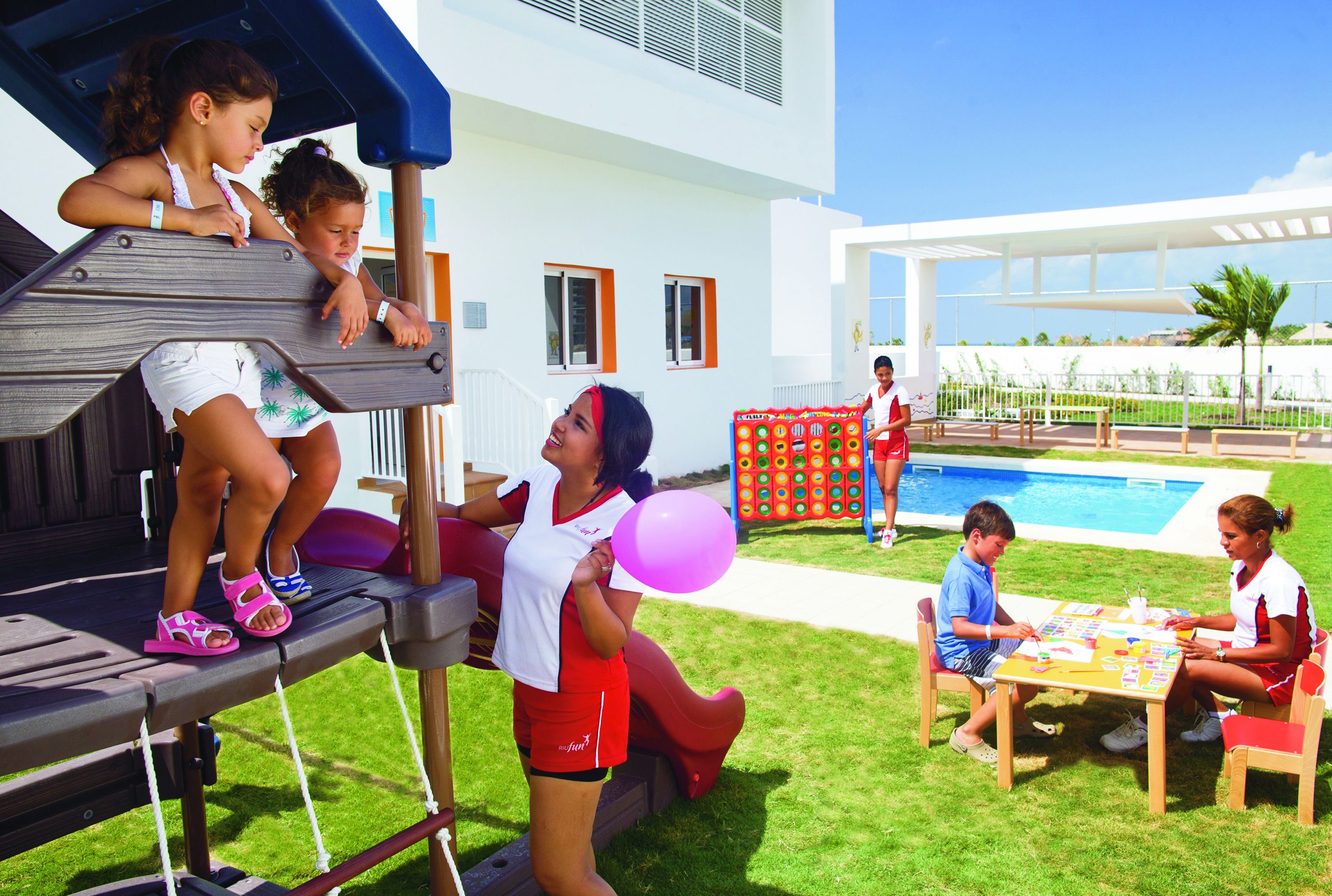 Un área de juegos al aire libre con un tobogán, una piscina y una mesa donde hay gente sentada.