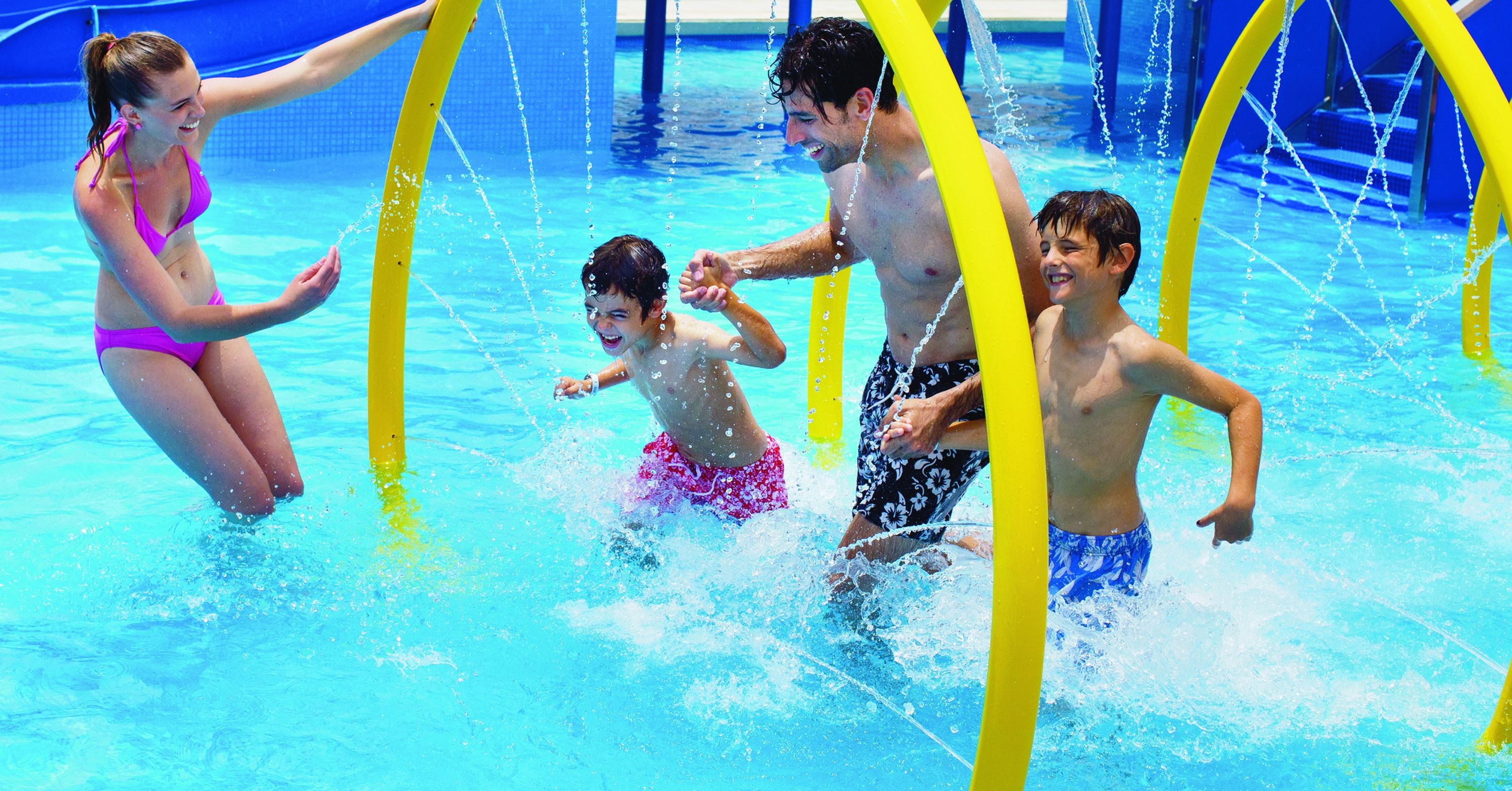 A swimming pool with clear blue water, yellow safety arches, and people enjoying the water.