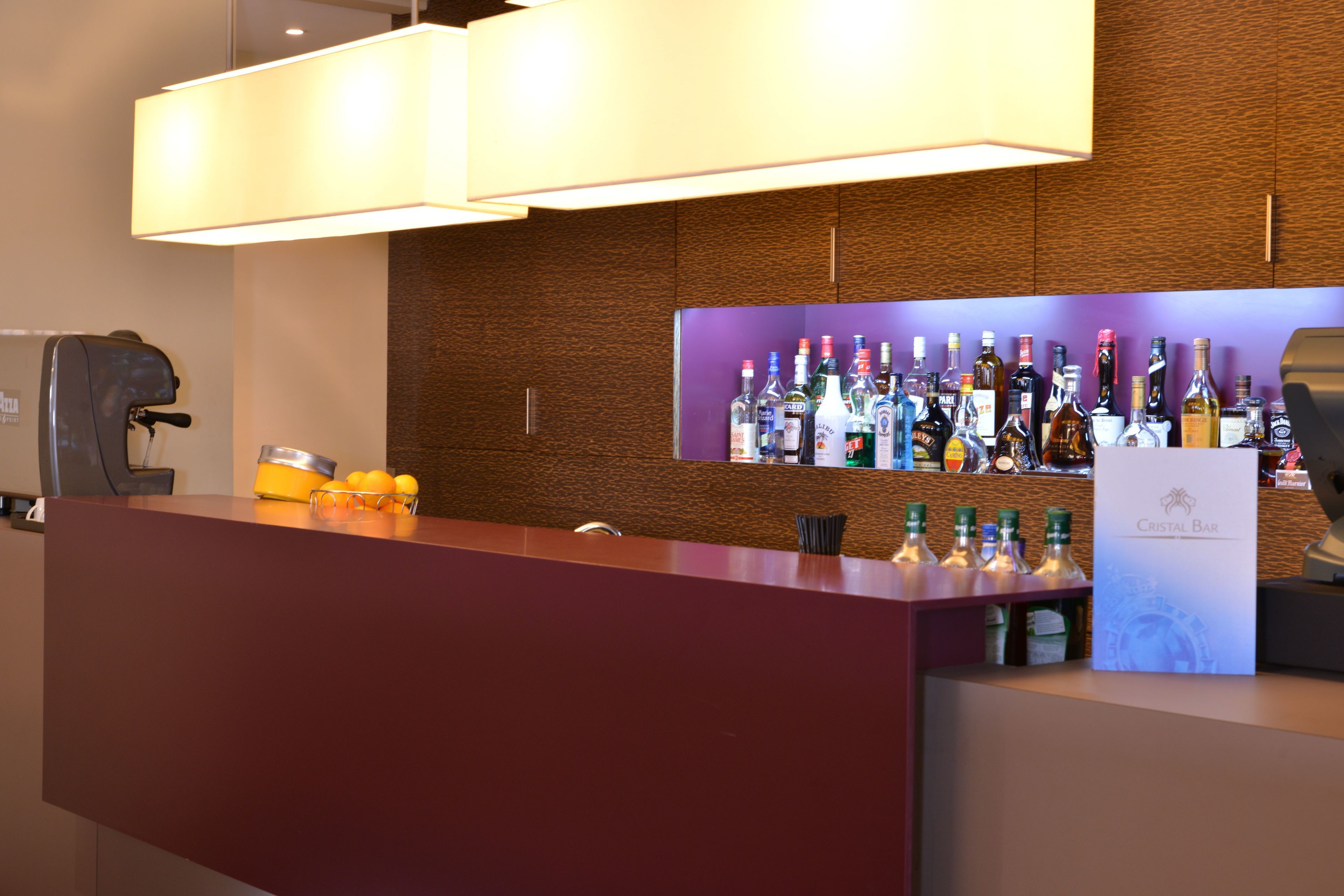 A bar area with a wooden wall and a purple shelf displaying various bottles.