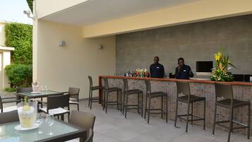 Uma área de bar ao ar livre com cadeiras de vime e painel de azulejos.