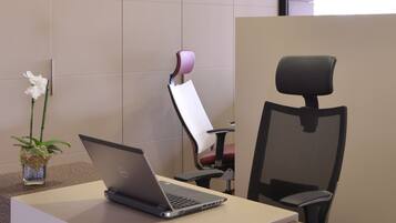 A laptop on a desk with a potted plant, two office chairs, and a partition wall.