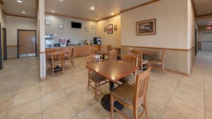 A dining area with wooden tables and chairs, a kitchen in the background, and framed pictures on the walls. - Econo Lodge Inn & Suites Bridgeport (Bridgeport)