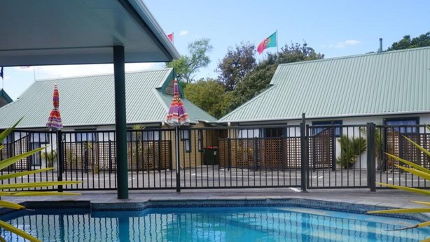 A swimming pool with a fenced area, a covered seating area, and a building with a metal roof. - Cheviot Park Motor Lodge (Whangarei)
