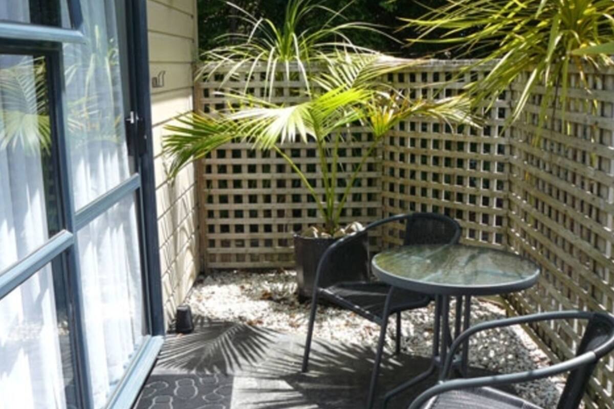 An outdoor patio with a glass door, a small round table, two chairs, and a wooden lattice fence.