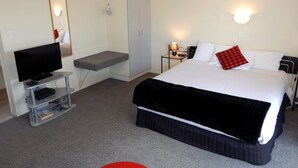 A hotel room with a bed, a television, a wardrobe, and a small desk with a lamp. - Cheviot Park Motor Lodge (Whangarei)