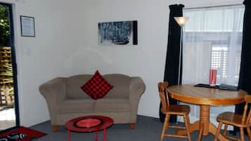 A living room with a beige sofa, a red and black checkered pillow, a small red table, and a wooden dining table with chairs.