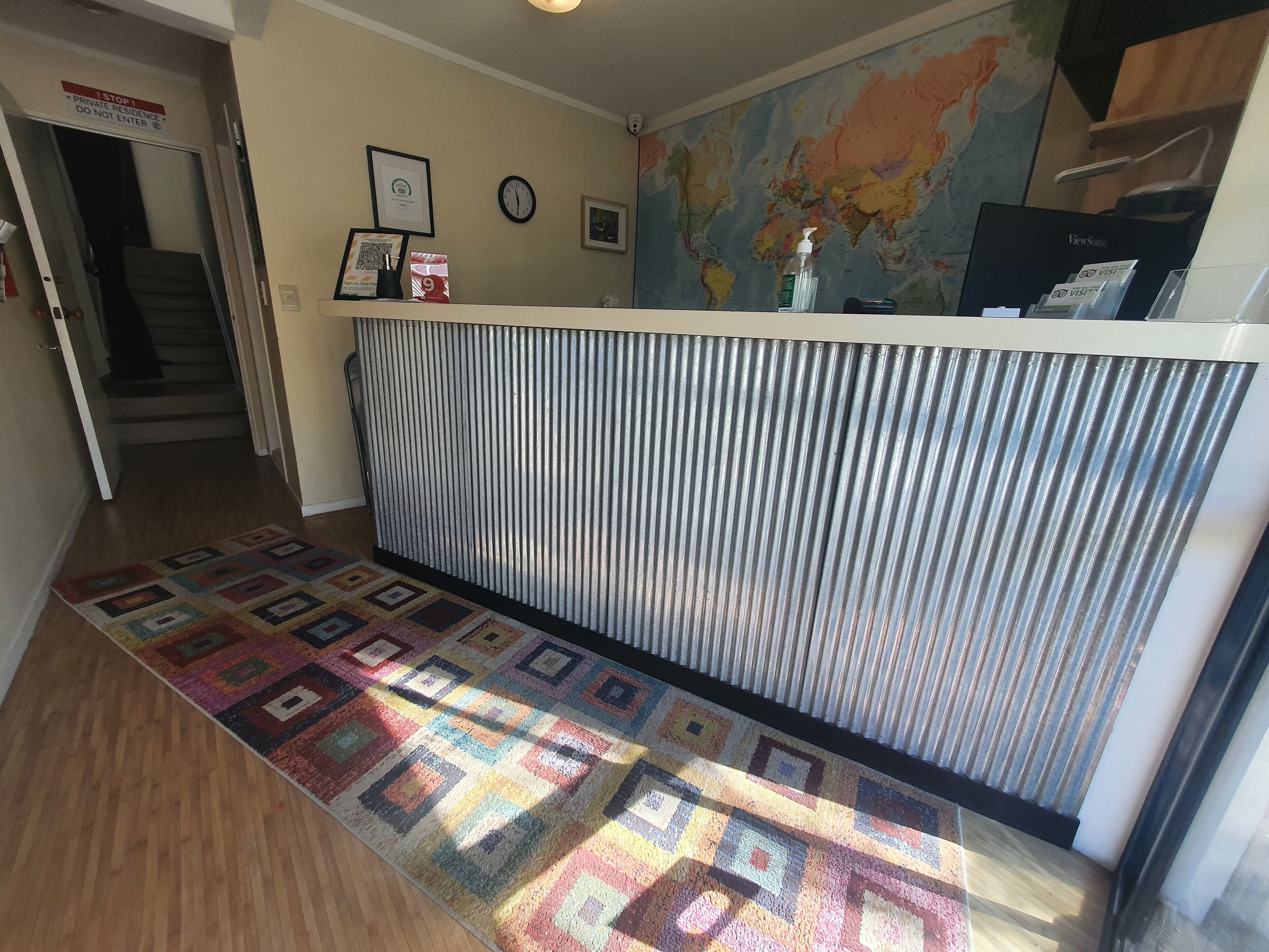 Une salle d'attente avec un tapis à motifs, une carte du monde accrochée au mur, des certificats encadrés et une horloge.